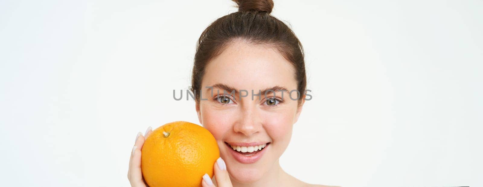 Vitamin C and health concept. Young beauty woman, holding orange fruit near face, concept of organic skincare treatment, facial and body products, standing over white background by Benzoix