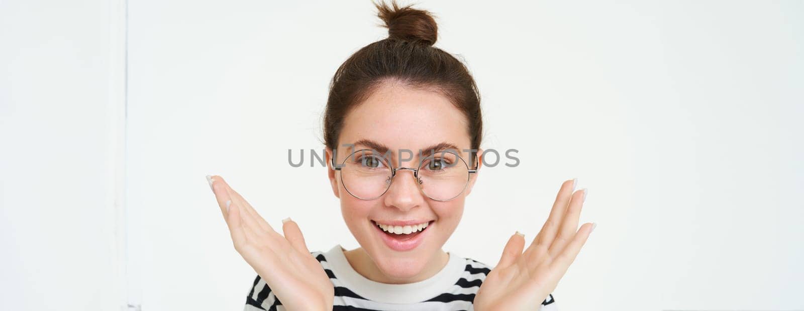 Close up portrait of amazed, happy young woman in glasses, clasp hands, applause, clapping and smiling, standing over white background.