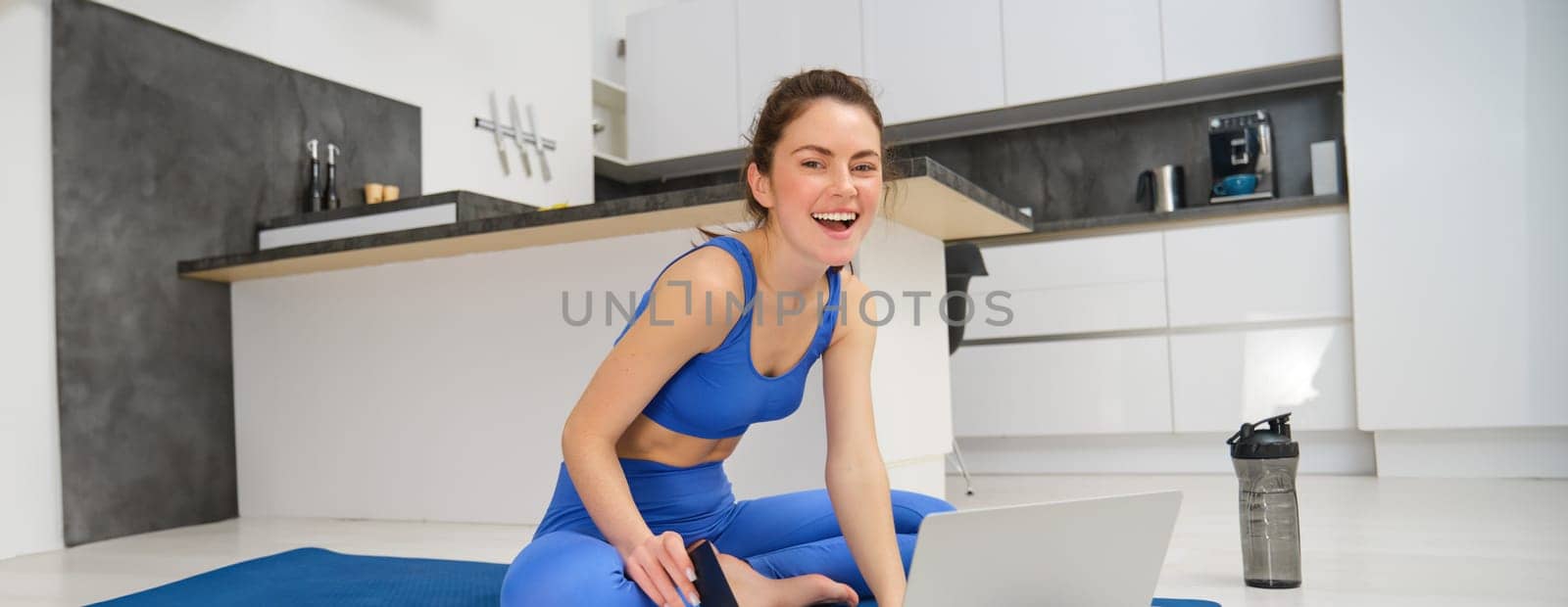 Image of young sportswoman, fitness girl watching online yoga tutorial on laptop and exercising, following video instructions by Benzoix