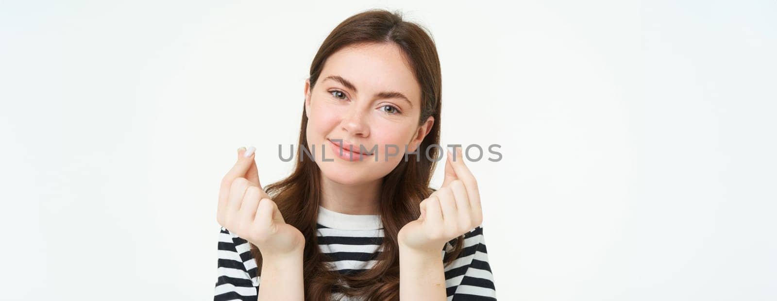 Portrait of beautiful young woman shows finger hearts sign, love and care, likes smth, stands over white studio background.