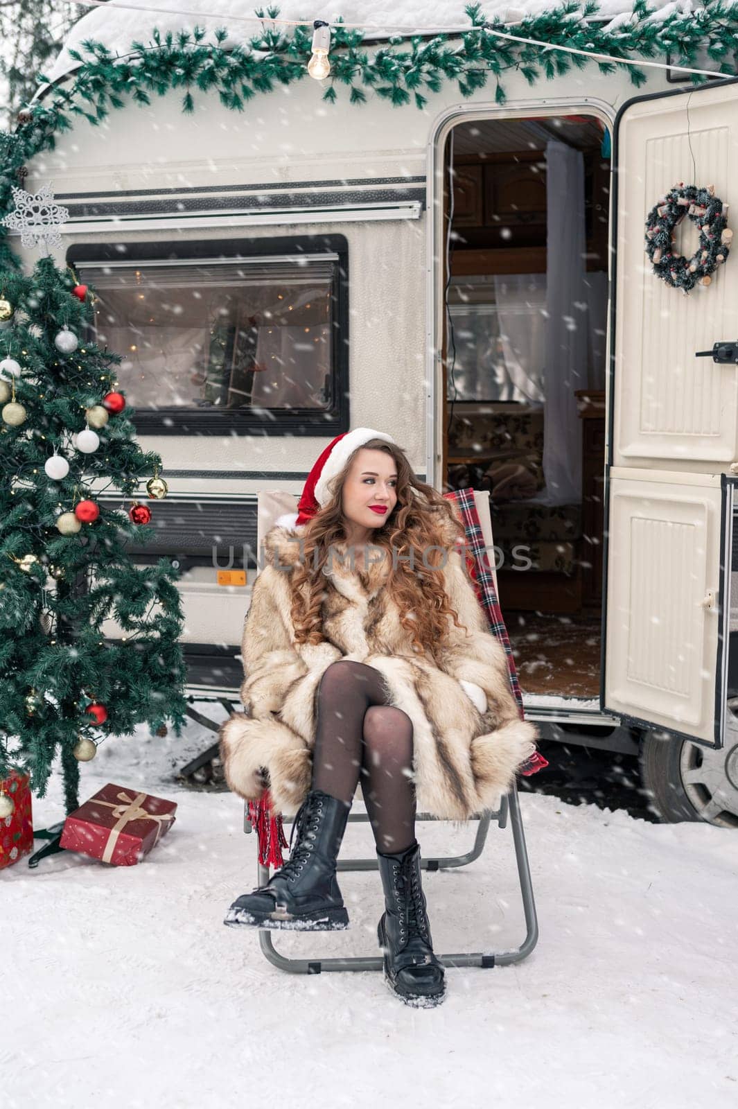 Young woman in santa costume resting at winter campsite. New year celebration concept