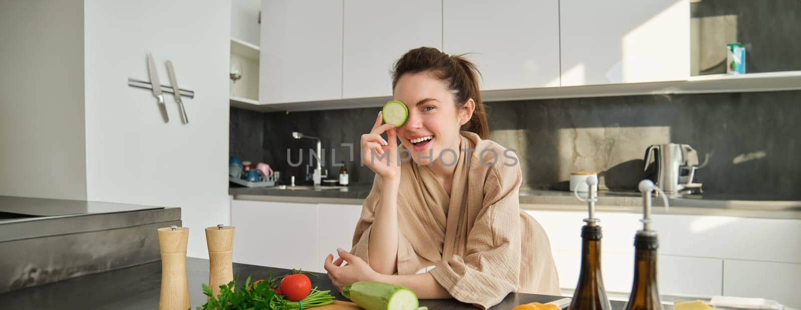 Portrait of brunette woman, wife cooking at home, making dinner, posing near chopping board in kitchen with vegetables, holding zucchini by Benzoix