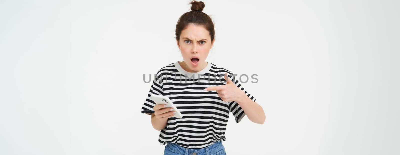 Angry woman complaining, pointing at smartphone and shouting with frustrated face expression, isolated over white background.