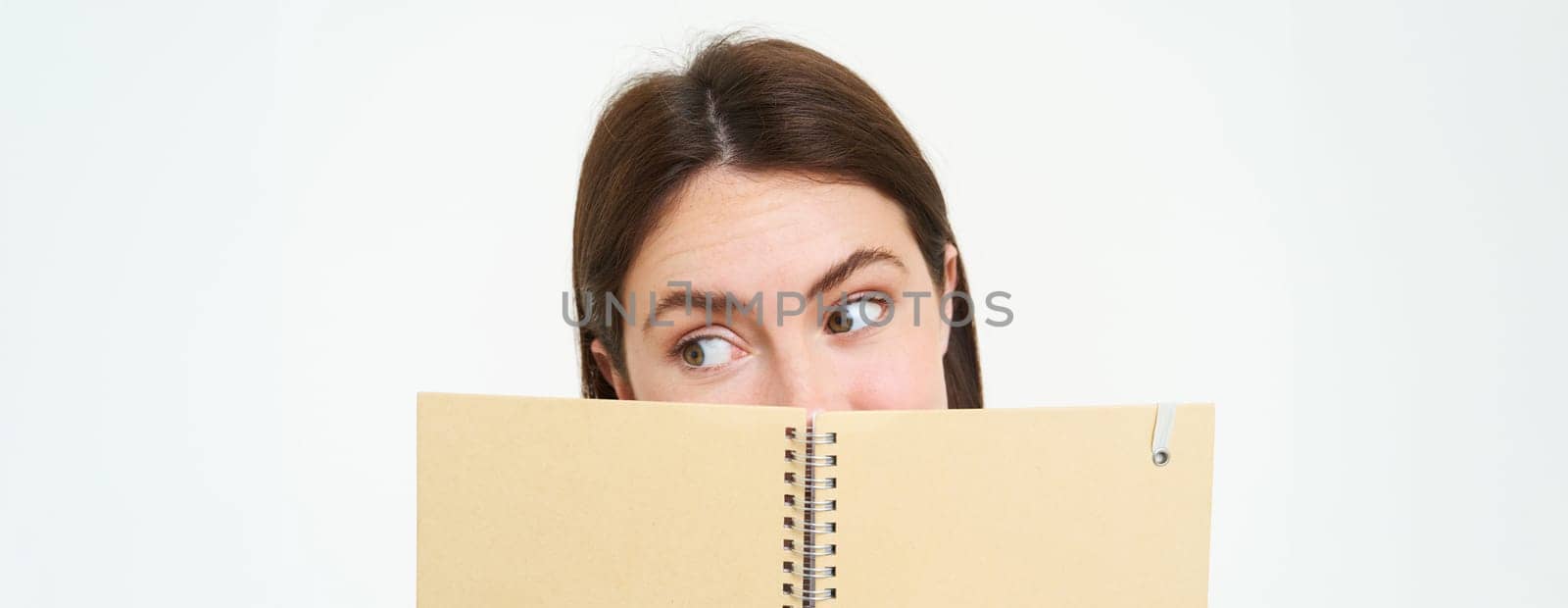 Image of woman reading something interesting in notebook, holding planner and making a side eye, standing over white background.