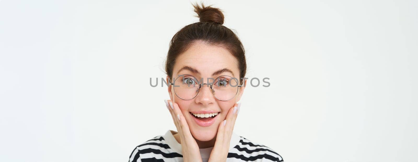 Image of amazed, smiling young woman in eyewear, wearing glasses, looking impressed and excited, standing over white background by Benzoix