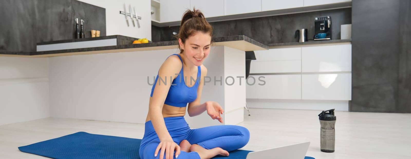 Portrait of fit, smiling fitness instructor, woman talking to laptop, discussing workout exercises with client, giving online yoga lesson via video chat.