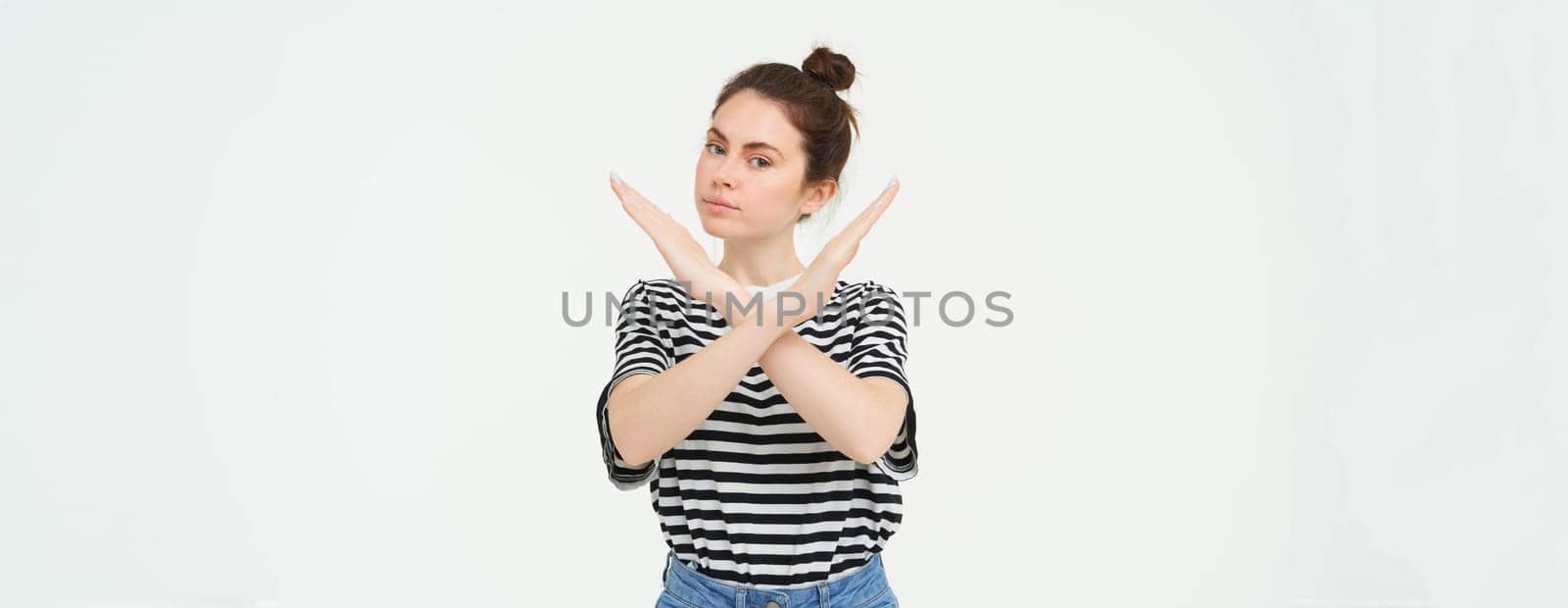 Portrait of confident young woman, showing cross sign, prohibit gesture, disapprove something, isolated against white background.
