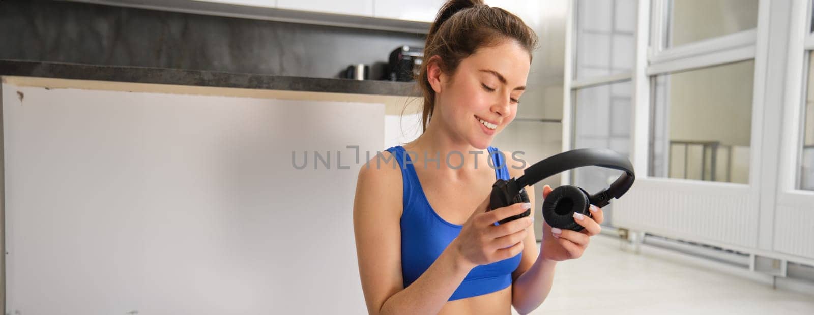Portrait of woman in tracksuit, doing yoga training, workout at home with wireless headphones, listening music to focus.