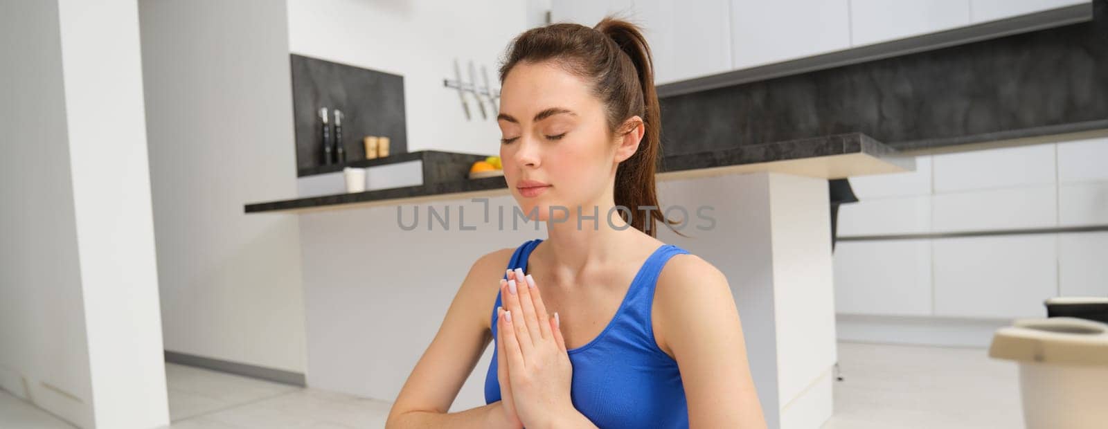 Woman practicing yoga and meditation at home sitting in lotus pose on yoga mat, relaxed with closed eyes. Mindful meditation concept. Wellbeing.