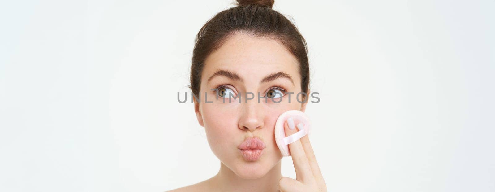 Portrait of woman washing off her face, takes off makeup with cosmetic pad, puts on skincare cleanser, stands over white background by Benzoix