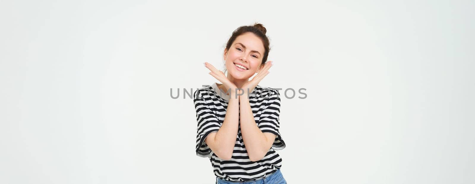 Wellbeing and women concept. Portrait of young woman with cute face, holds hands near head and smiles, isolated against white background by Benzoix