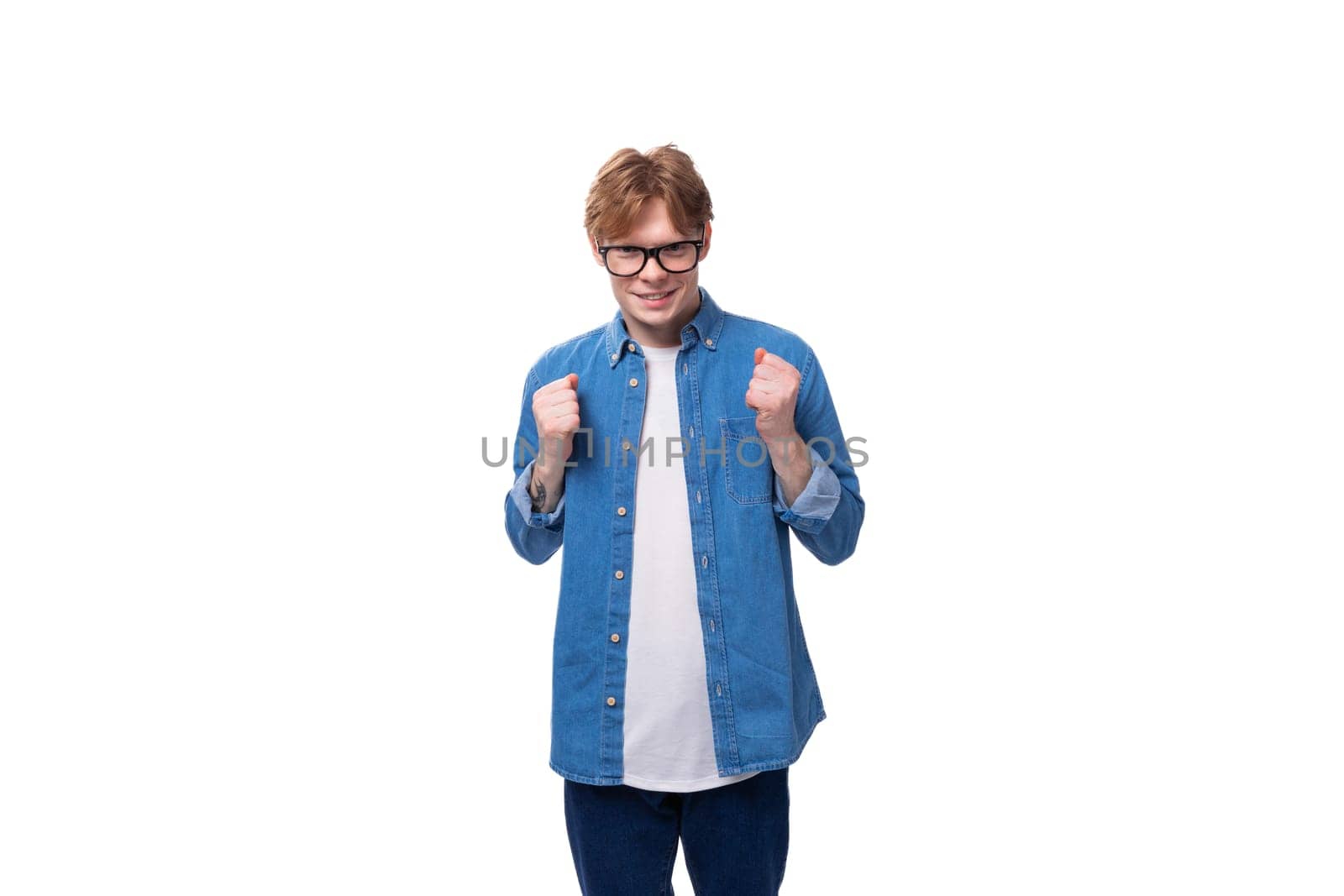 young handsome caucasian man with short red hair dressed in a blue shirt on a white background with copy space by TRMK