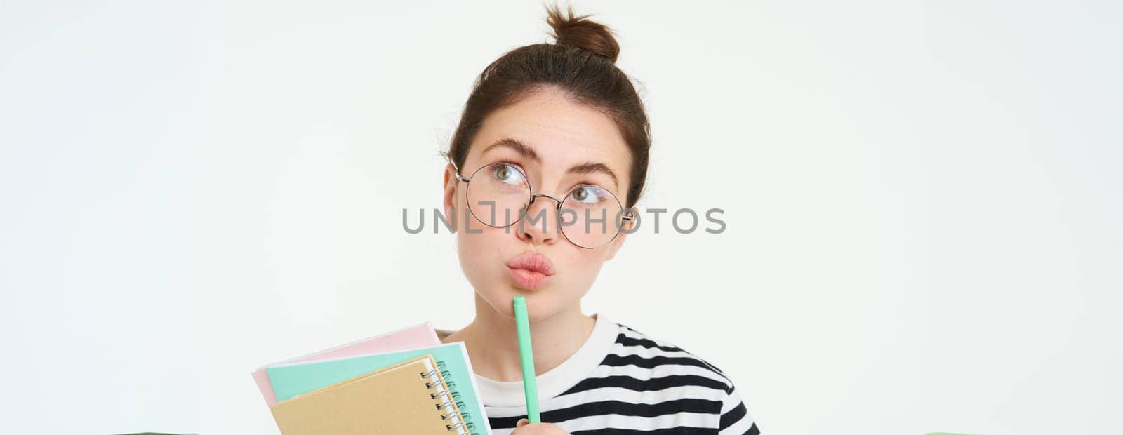 Close up portrait of girl in glasses, thinking, holding notebook and pen, looking up and pondering, making decision, standing over white background.