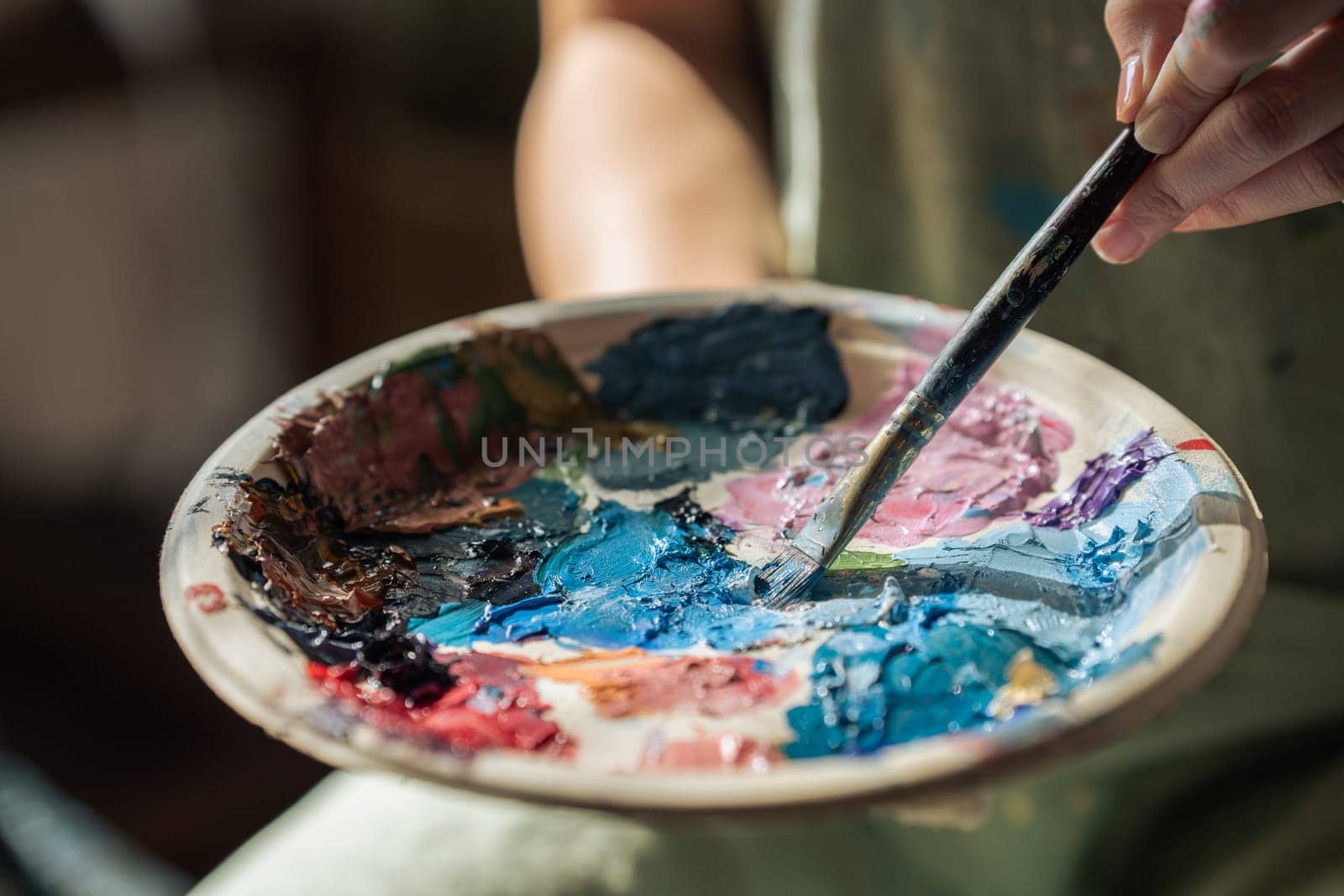 artist brush mix color painting on palette is holding in his hand closeup.