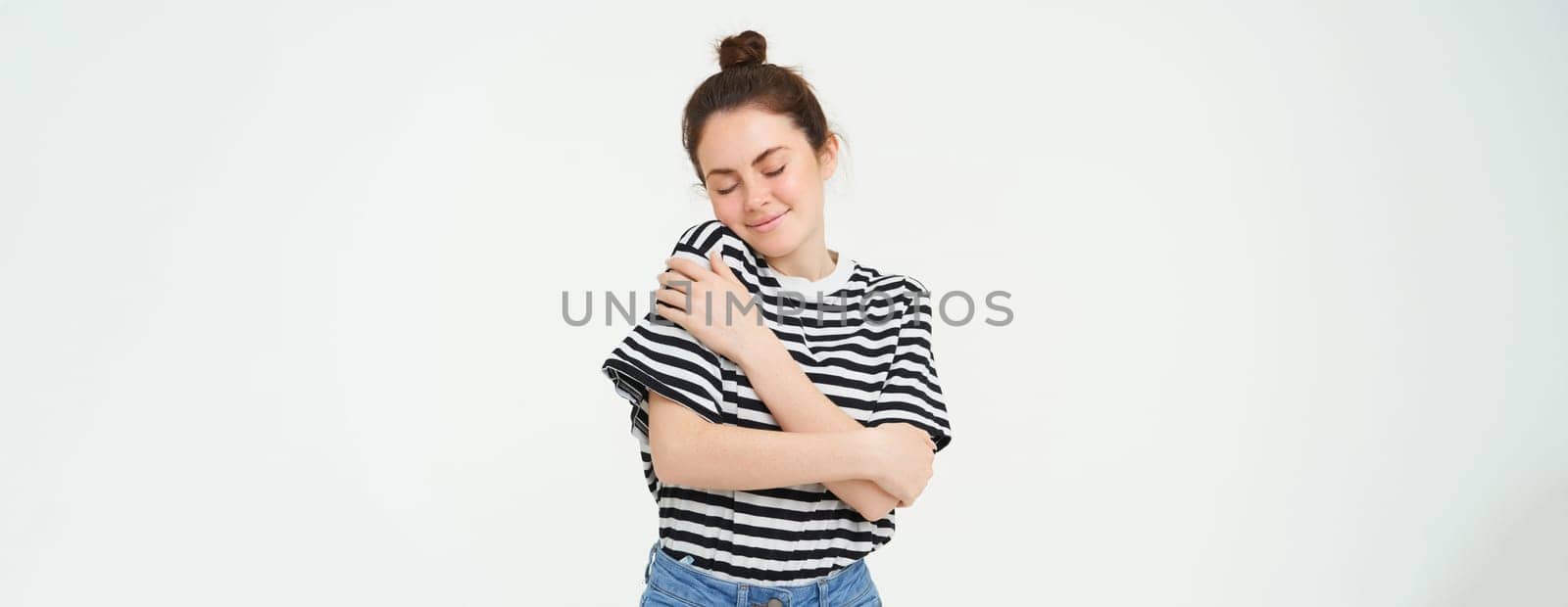 self-care and love. Young beautiful woman hugs herself, embraces own body and smiles, stands over white background.