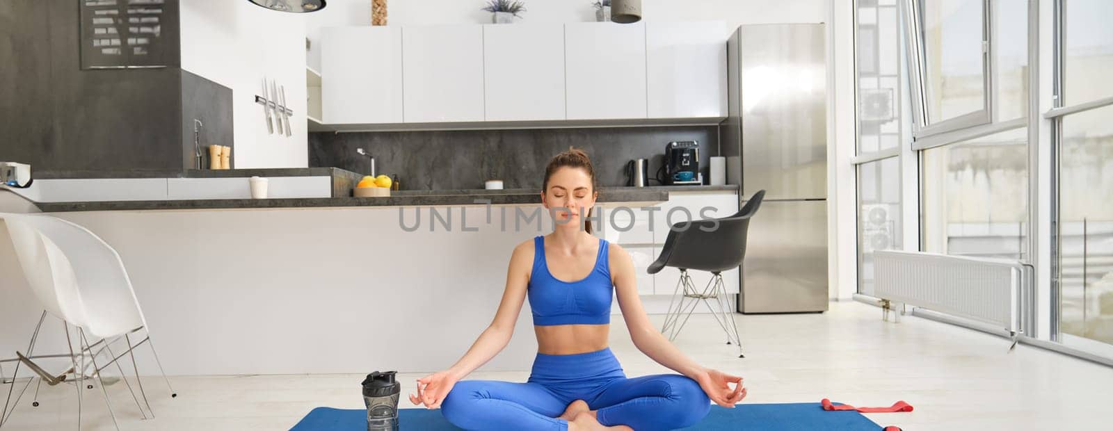 Fitness and mindfulness. Young woman doing yoga, sitting at home and meditating, close eyes and sits in asana pose on rubber mat.