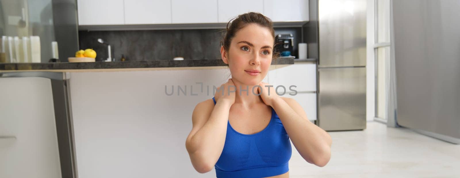 Close-up potrait of fitness woman, does training, workout from home, massaging neck, exercise in living room by Benzoix