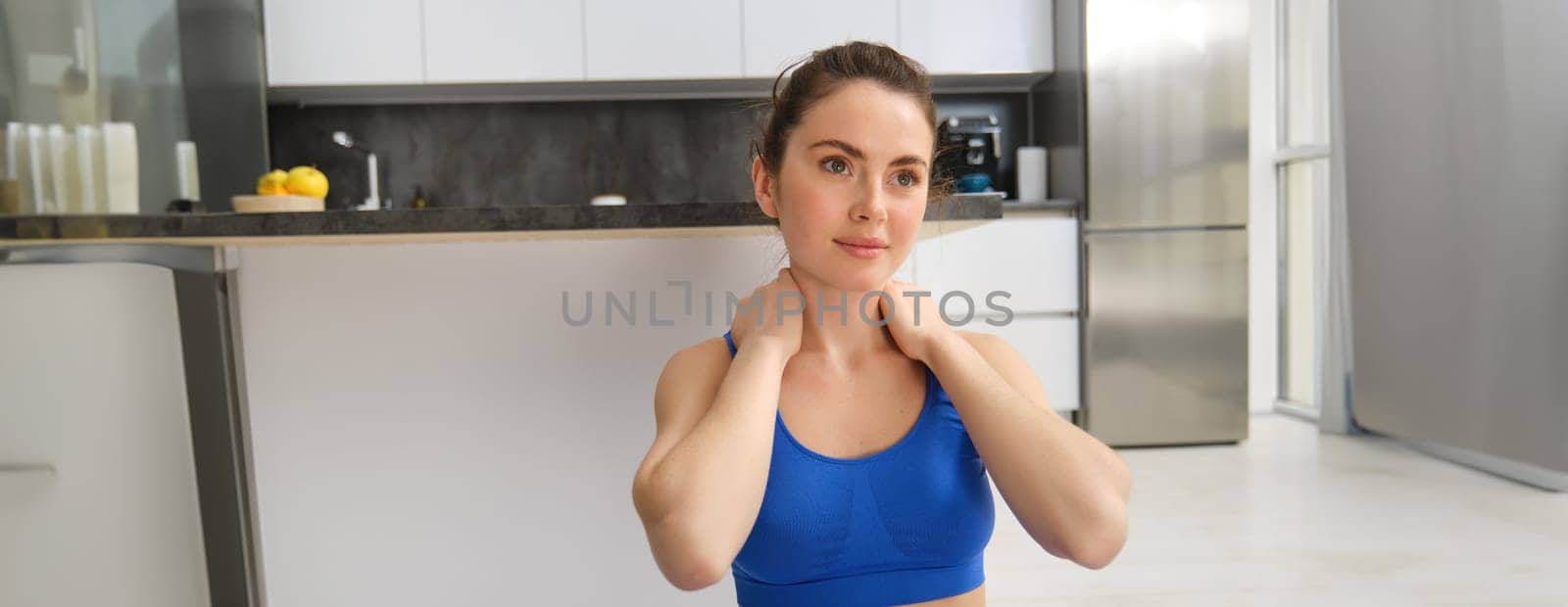 Close-up potrait of fitness woman, does training, workout from home, massaging neck, exercise in living room. Sport and wellbeing concept