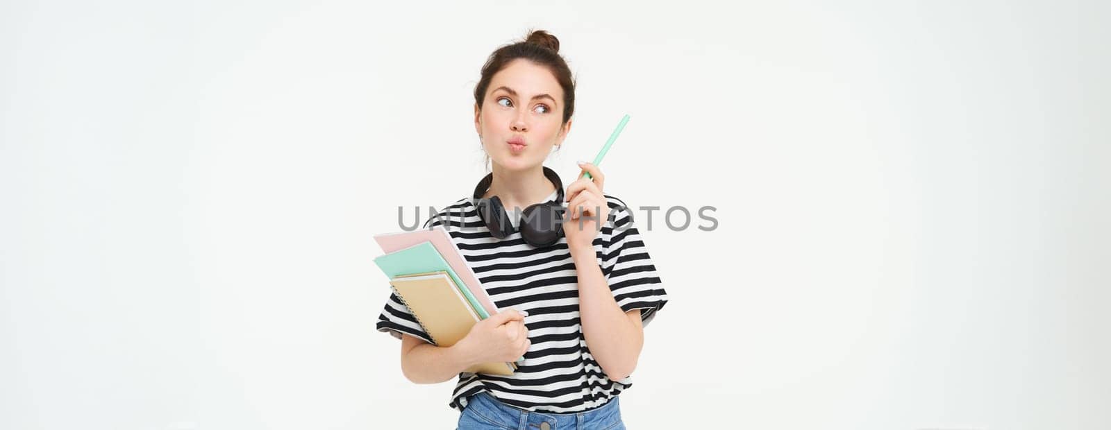 Portrait of young woman standing with books, student looking thoughtful at copy space, thinking about something, holding notebooks and homework in hands, white background by Benzoix