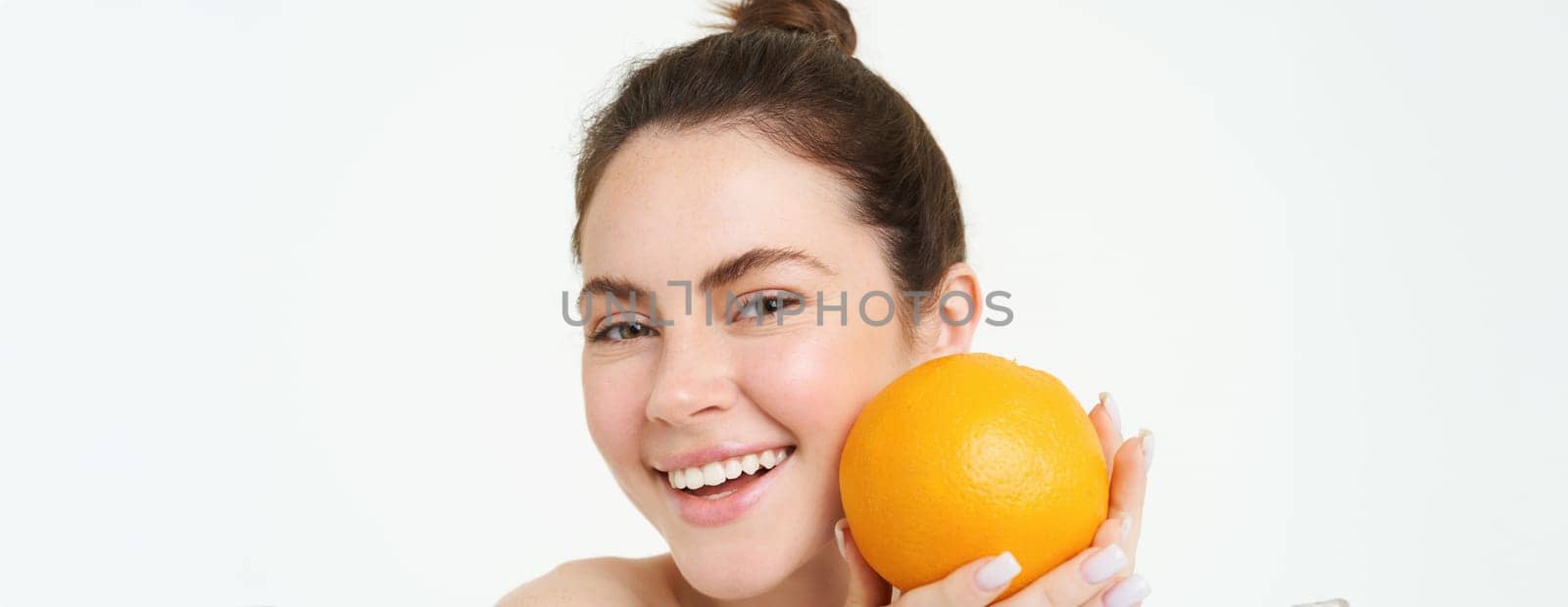 Vitamin C and health concept. Young beauty woman, holding orange fruit near face, concept of organic skincare treatment, facial and body products, standing over white background.