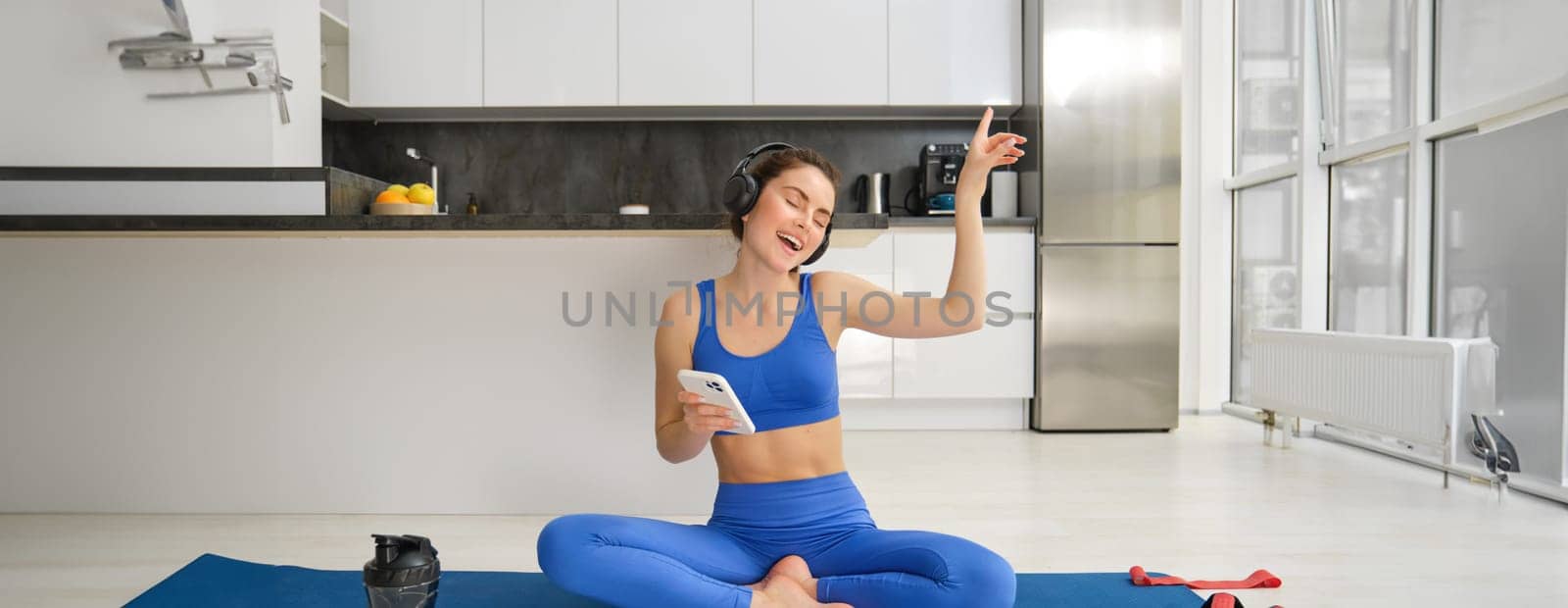 Dancing happy woman, workout from home on rubber yoga mat, having fun while training alone indoors with music by Benzoix