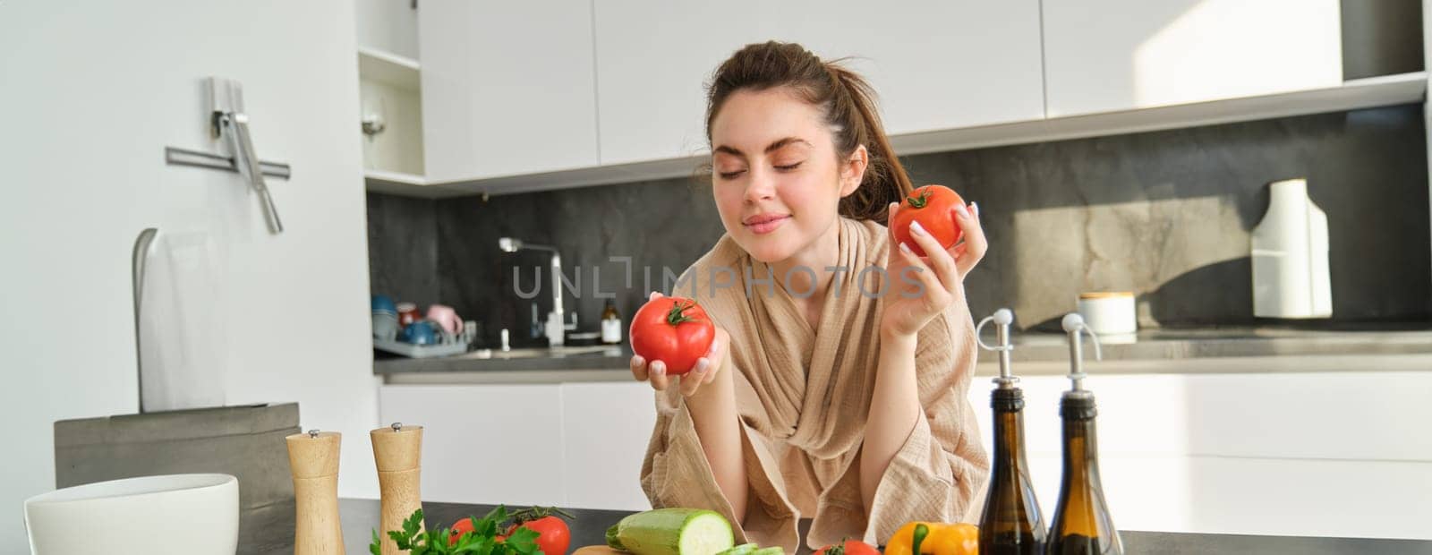 Portrait of woman cooking at home in the kitchen, holding tomatoes, preparing delicious fresh meal with vegetables, standing near chopping board by Benzoix