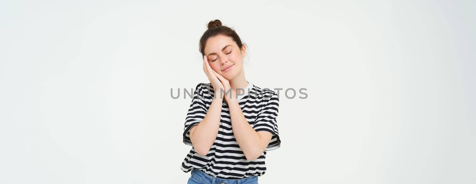 Image of tender woman, 25 years, holds hands near face and closes eyes, sleeps, smiles pleased during nap, isolated against white background.
