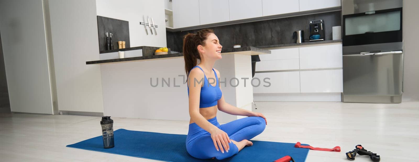 Image of woman does yoga practices from home, sits on rubber mat and meditating, workout in living room, concentrating on breathing exercises by Benzoix