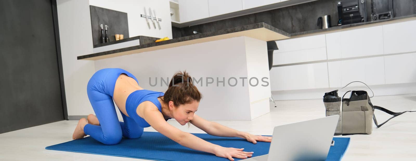 Image of young sportswoman, fitness girl watching online yoga tutorial on laptop and exercising, following video instructions.