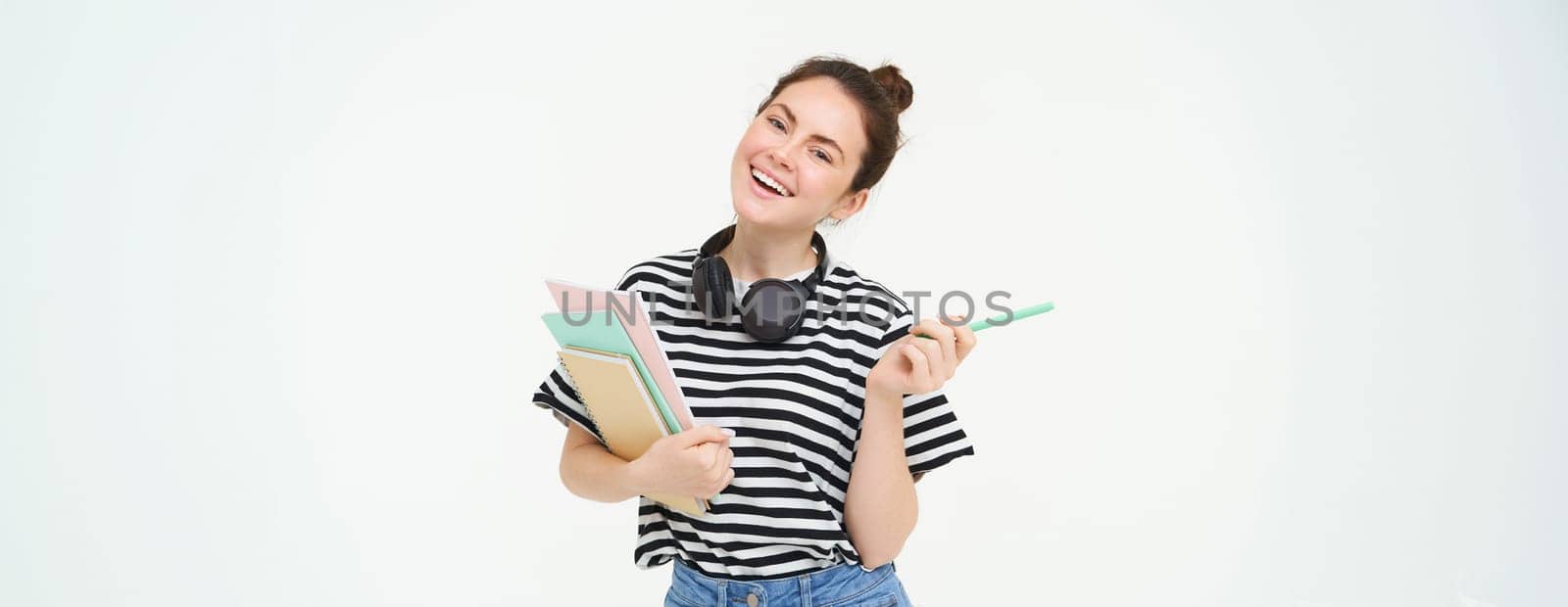 Portrait of young woman, student with notebooks and earphones on her neck, posing for college advertisement, white background by Benzoix