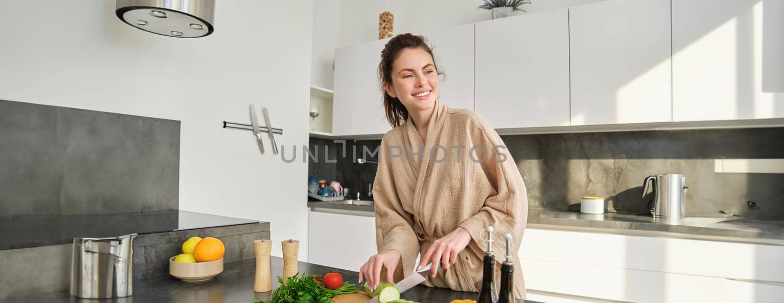 Portrait of beautiful brunette girl chopping vegetables for meal, making salad in the kitchen, eating healthy food, preparing dinner by Benzoix