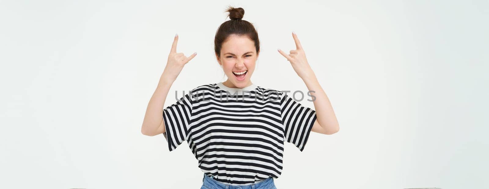 Portrait of excited young woman having fun, rock n roll gesture, enjoys concert, posing upbeat, standing over white background by Benzoix