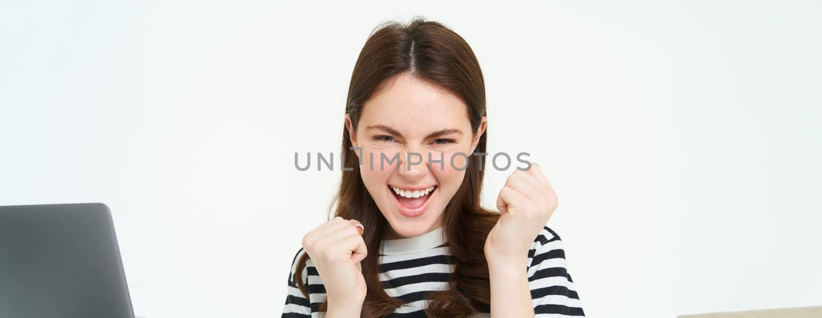 Portrait of beautiful young student, woman winning, shaking hands and say yes, cheering, rooting for team, celebrating victory, standing isolated on white background by Benzoix