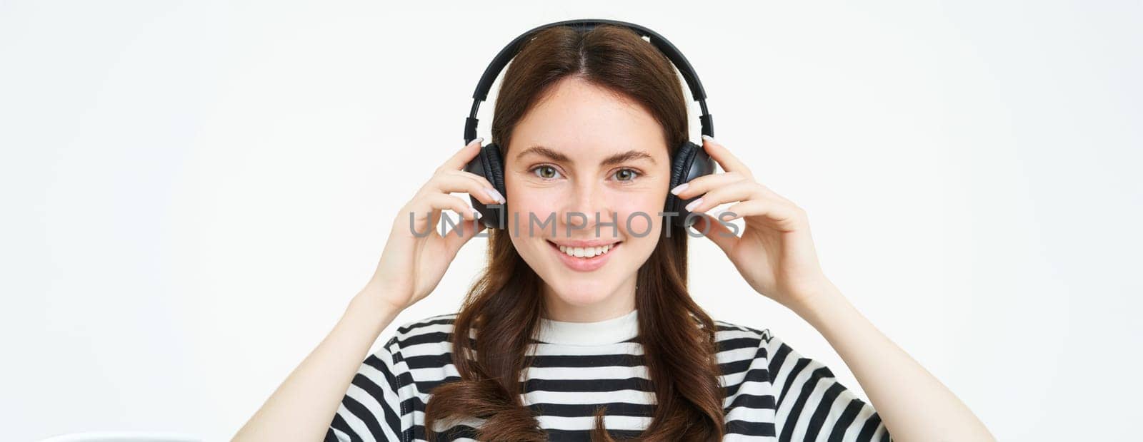Portrait of woman, smiling, wearing wireless headphones, listening music, studying in earphones, standing isolated over white background.