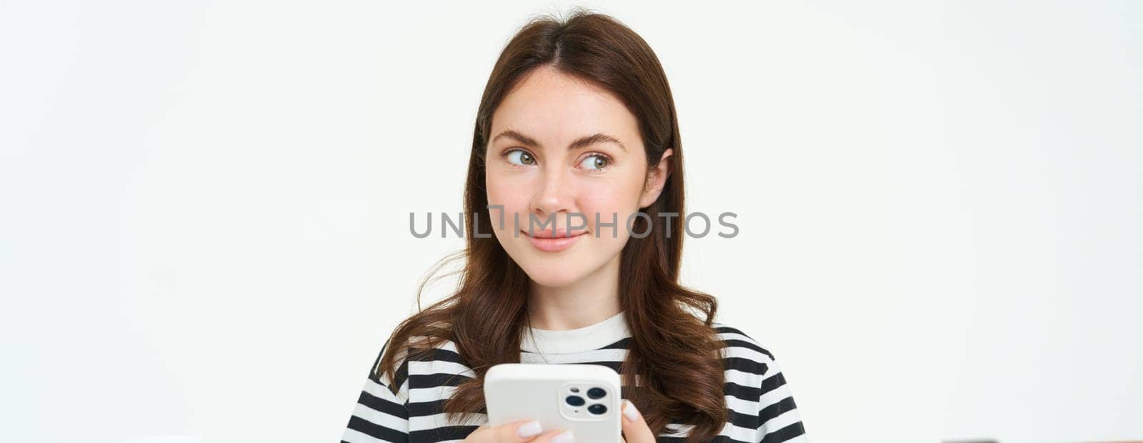 Portrait of girl with phone, woman holding smartphone and thinking, smiling and looking aside, deciding to buy smth online, white background.