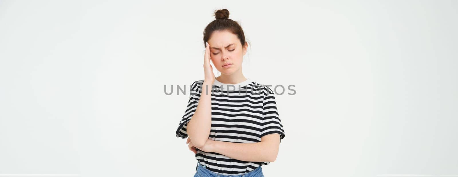 Portrait of tired woman rubs her forehead, touches head, has a headache, stands distressed against white background.