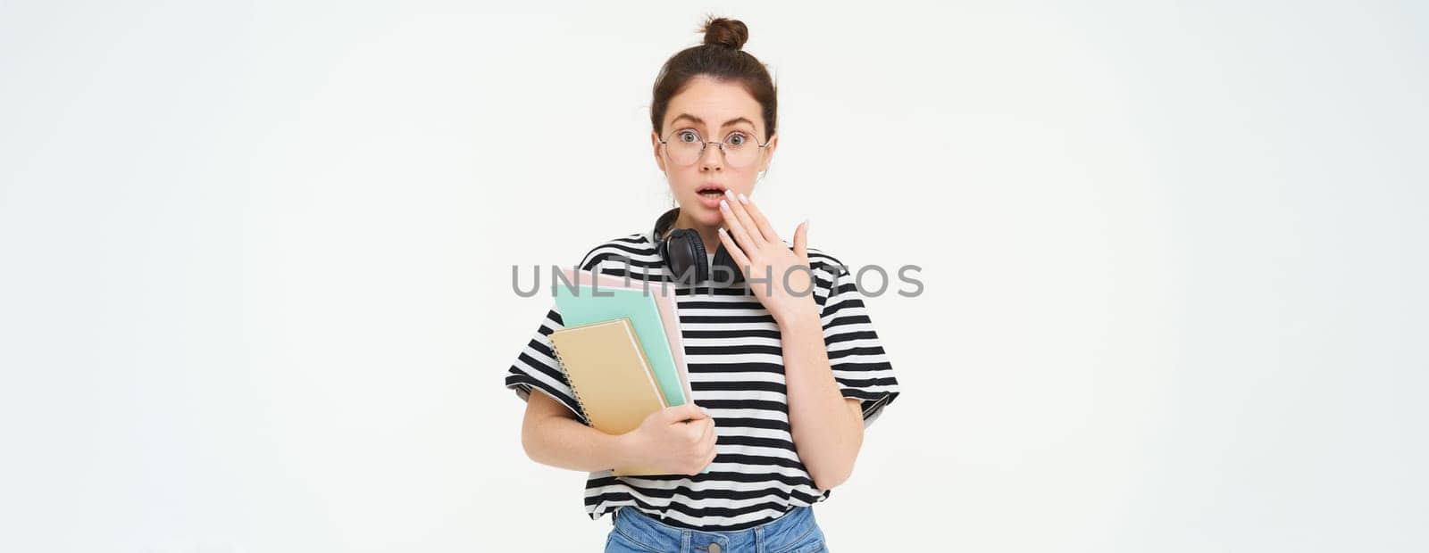 Portrait of woman in glasses, student looks surprised, gasps and looks shocked at camera, holds notebooks and study material, white background by Benzoix