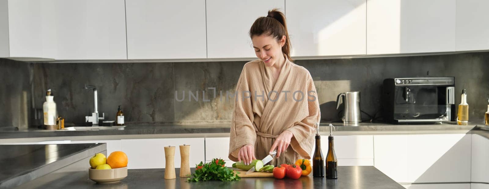 Portrait of woman cooking breakfast, chopping vegetables for salad, using board and knife, standing in the kitchen and wearing bathrobe by Benzoix