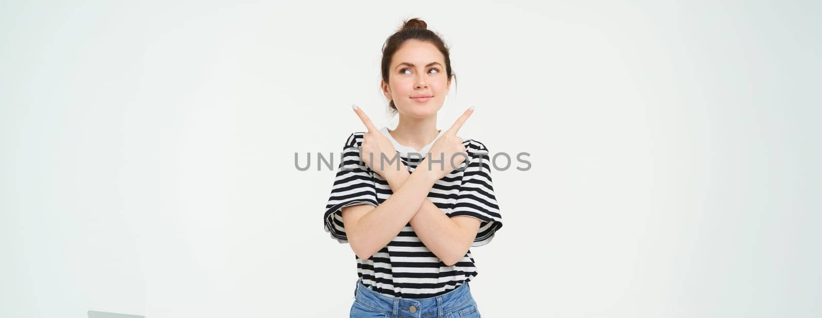 Portrait of beautiful, smiling young woman standing puzzled, makes choice, decides what to pick, points sideways left and right, stands over white background by Benzoix