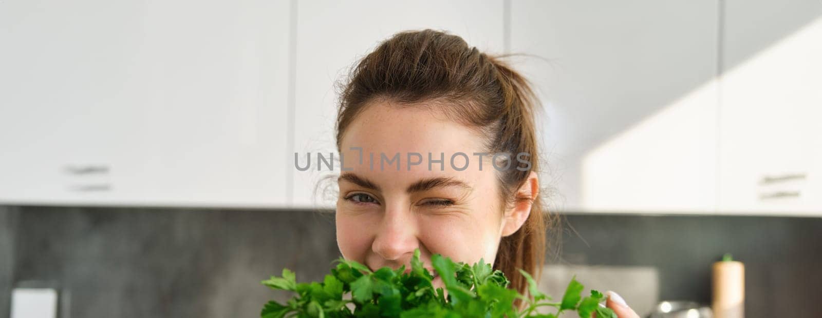 Portrait of beautiful woman cooking, holding fresh parsley, adding herbs while making salad, healthy meal in the kitchen by Benzoix