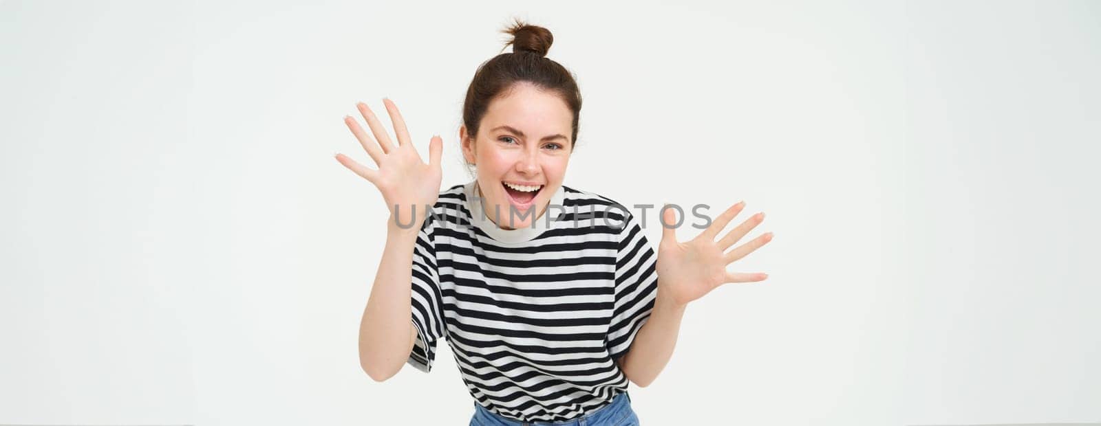Image of happy, beautiful young woman makes jazz hands, surprise gesture, posing in casual t-shirt and jeans over white background.