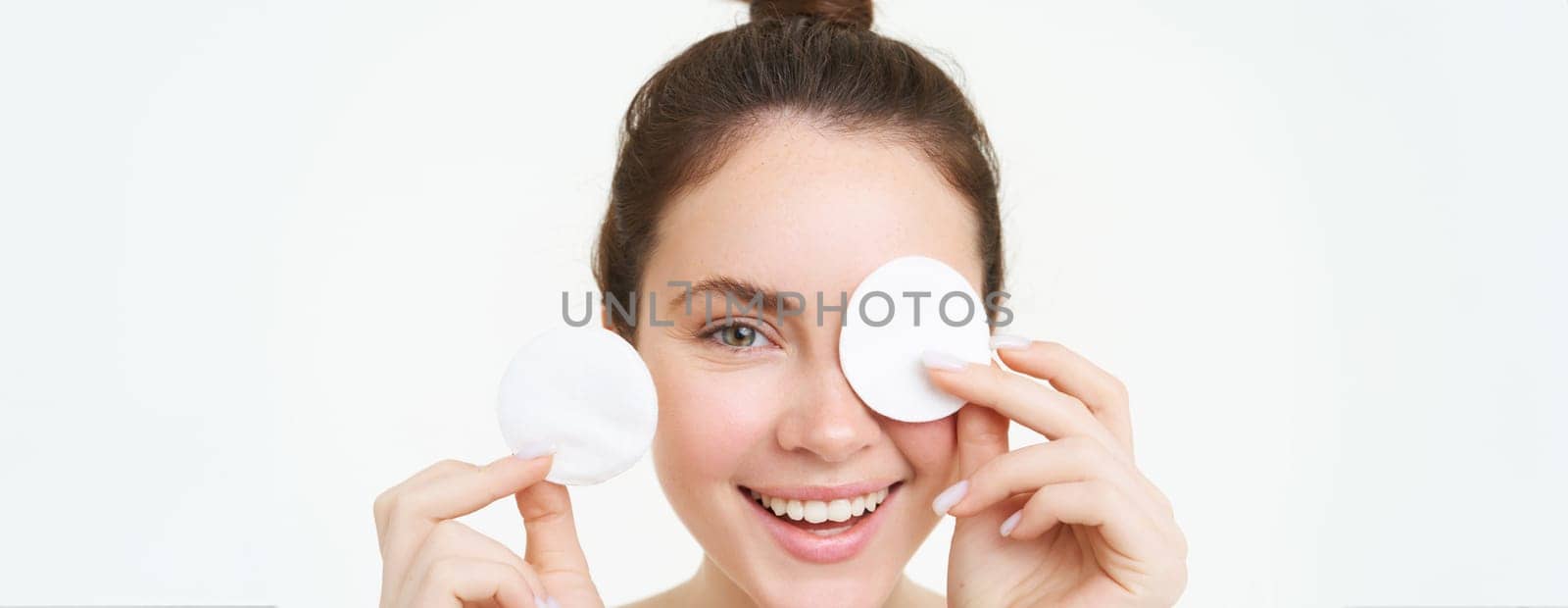 Beauty and female concept. Close up portrait, young woman holding cotton cosmetic pads near her face and smiling, removes makeup, uses daily facial cleanser, stands over white background.