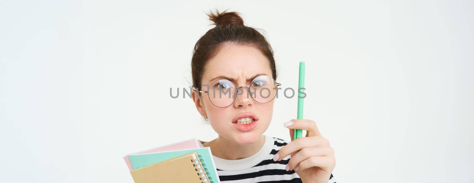 Portrait of angry woman in glasses, teacher scolding someone, shaking pen and arguing, holding notebooks, standing over white background.