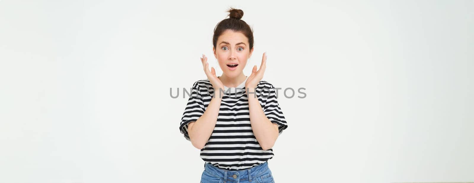 Portrait of surprised woman gasping, looking amazed, hear great news, drops jaw, says wow, impressed by something, stands over white background.