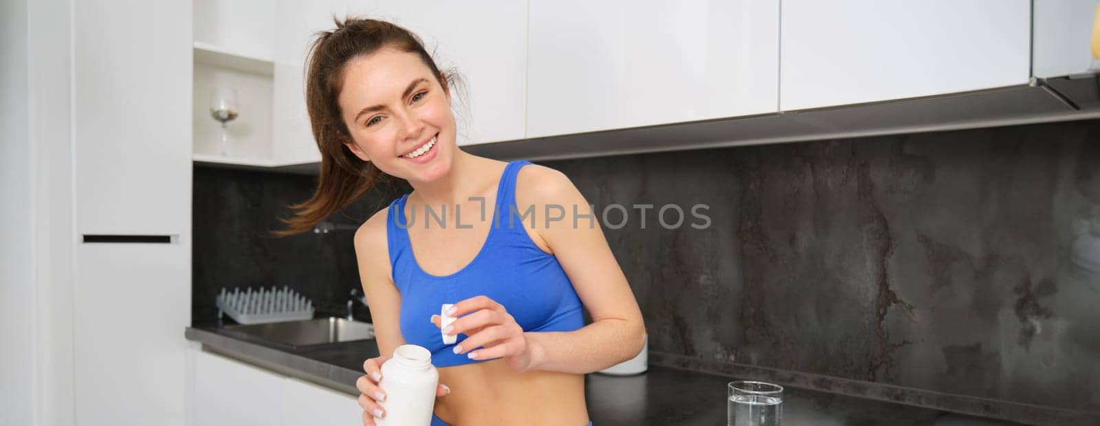 Portrait of brunette woman, wearing sport clothing, holding tablets, taking vitamins, dietary supplements buds for strong muscles, better workout results.