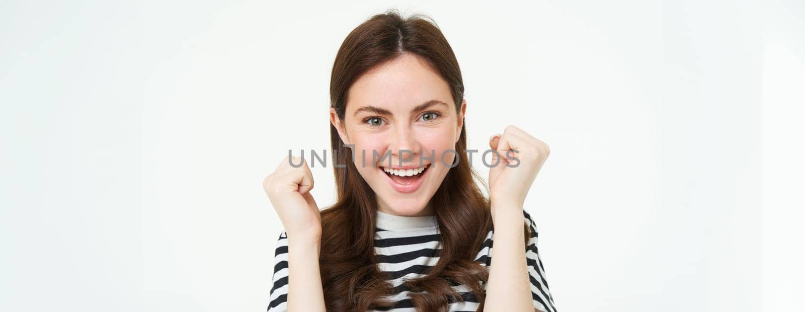 Excited young woman celebrating, shaking hands and looking happy, emotion of winning, triumphing, isolated on white background.