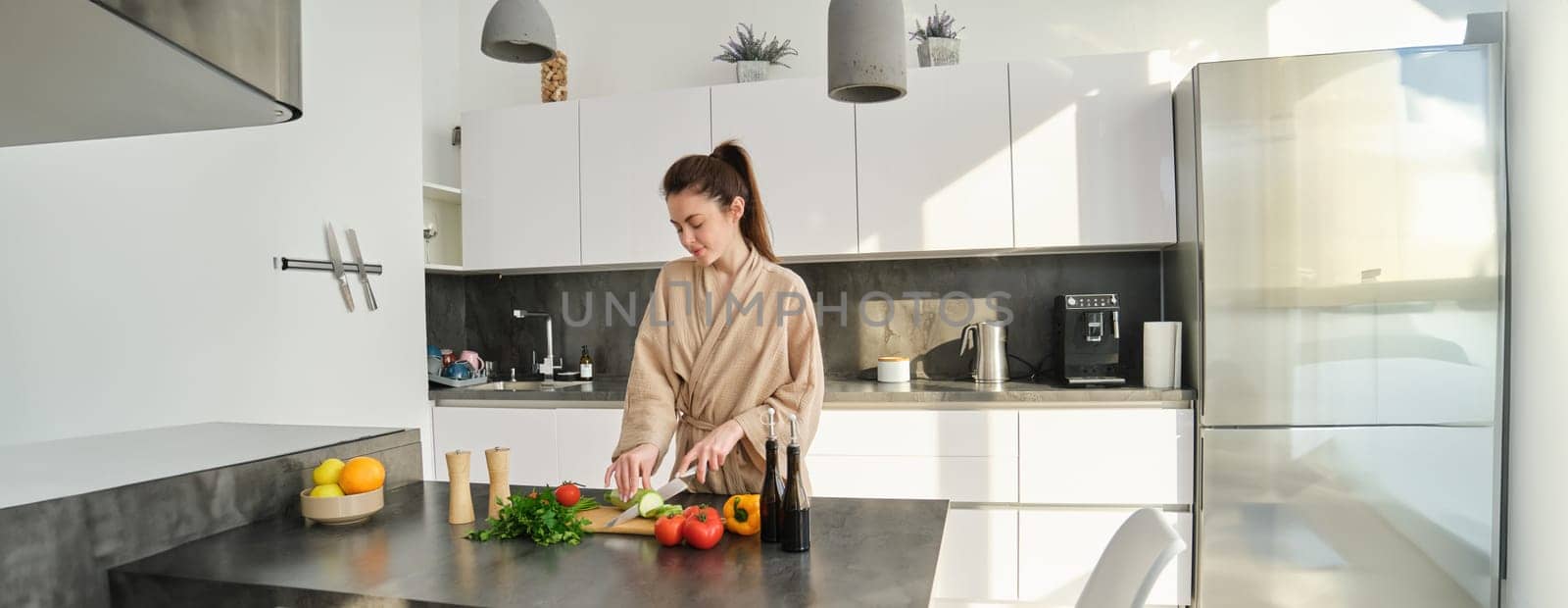 Portrait of beautiful brunette girl chopping vegetables for meal, making salad in the kitchen, eating healthy food, preparing dinner.