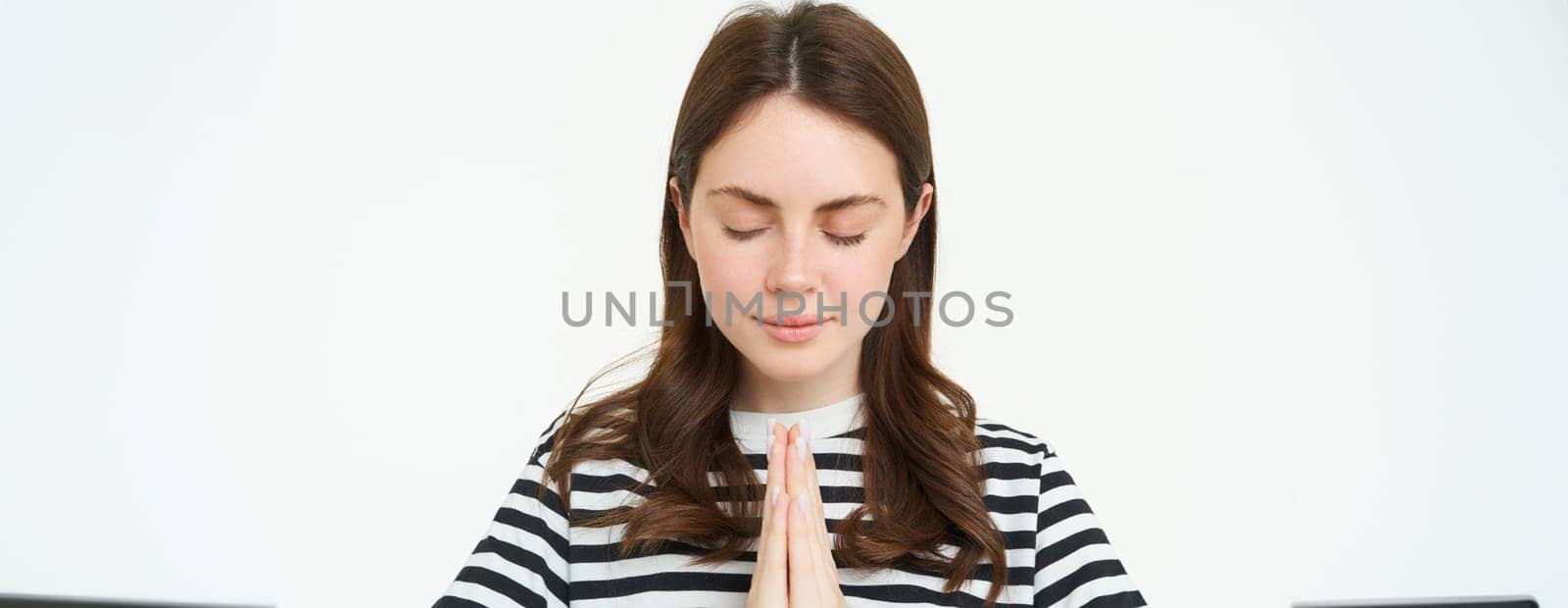 Portrait of woman showing namaste gesture, holding palms clenched together near chest, standing isolated over white background by Benzoix