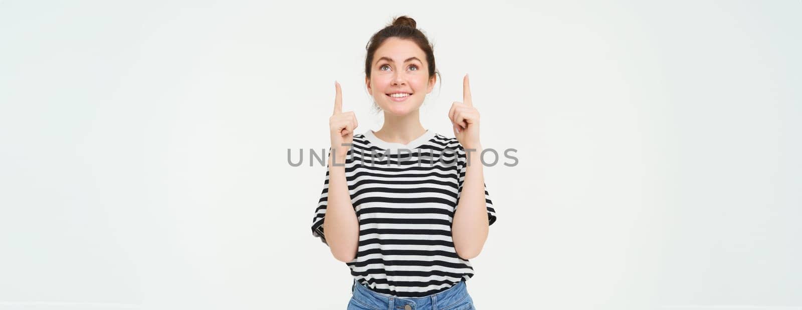 Portrait of excited, smiling young woman, looking and pointing up with happy, emotional face, white background by Benzoix