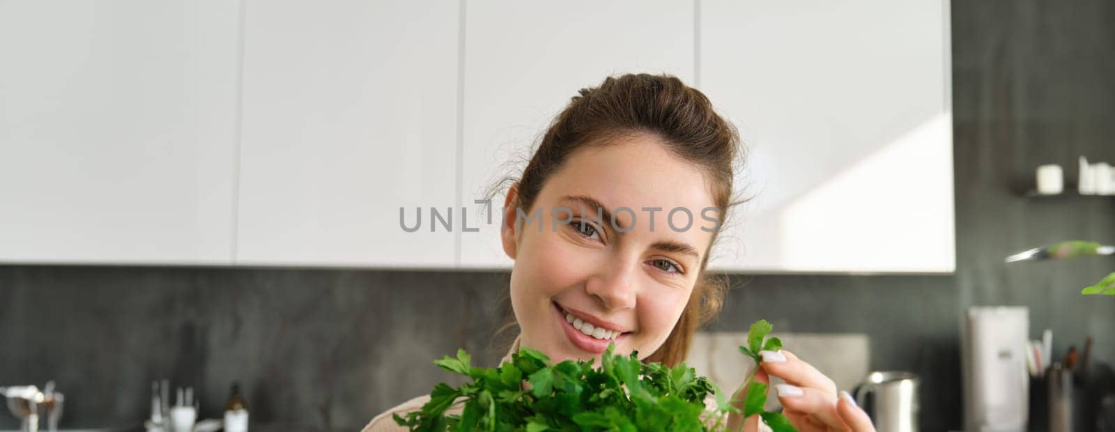 Portrait of beautiful woman cooking, holding fresh parsley, adding herbs while making salad, healthy meal in the kitchen.